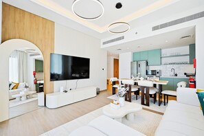 Una sala de estar moderna con un televisor de pantalla plana, muebles blancos y una cocina con gabinetes color aguamarina.