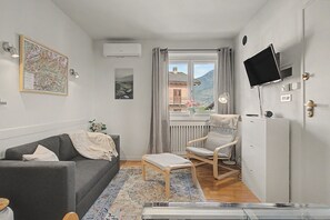 A compact living space with a grey sofa, a wooden rocking chair, a small table, and a TV mounted on the wall.