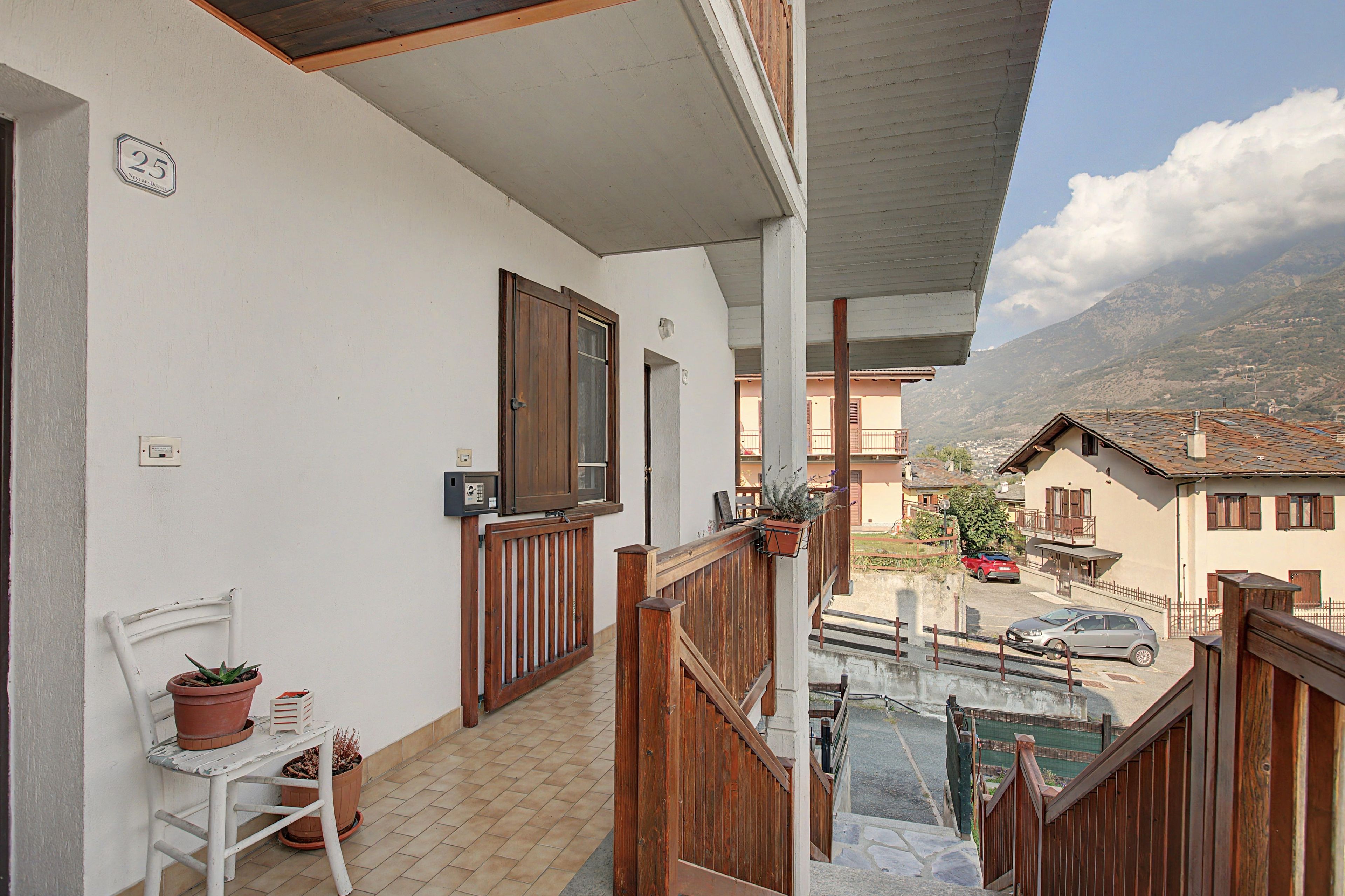 Ein Balkon mit Holzgeländer, Topfpflanzen und Blick auf einen Berg.
