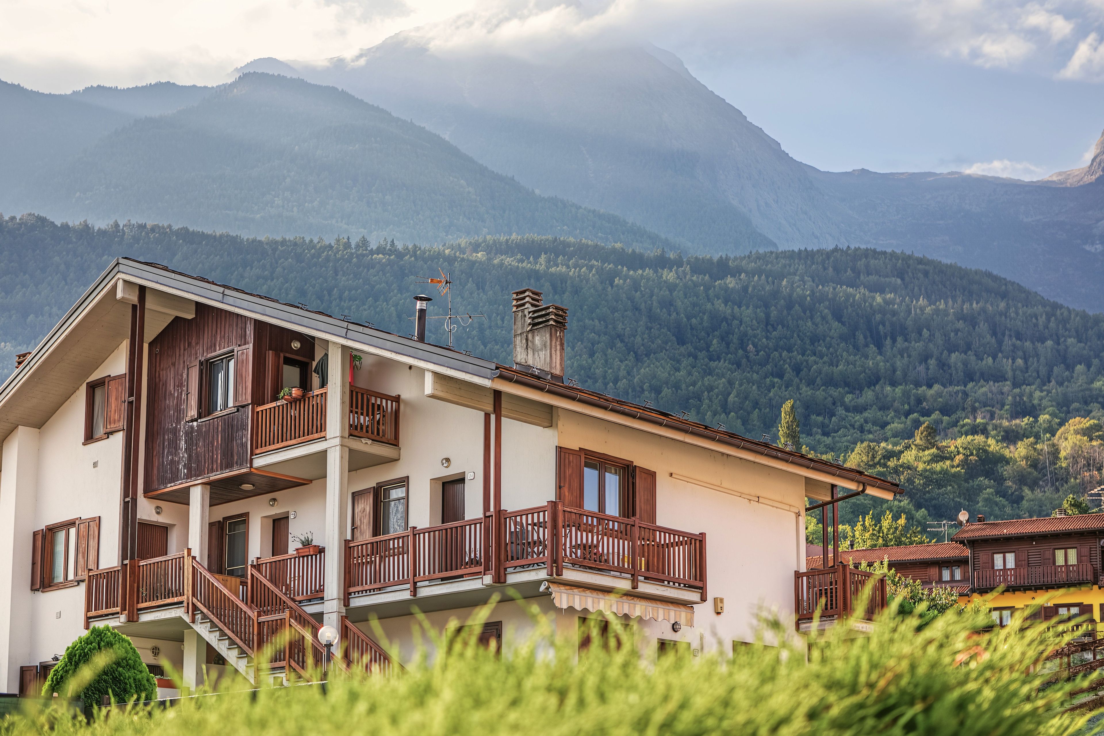 A two-story building with a balcony, a chimney, and a view of a mountain range.