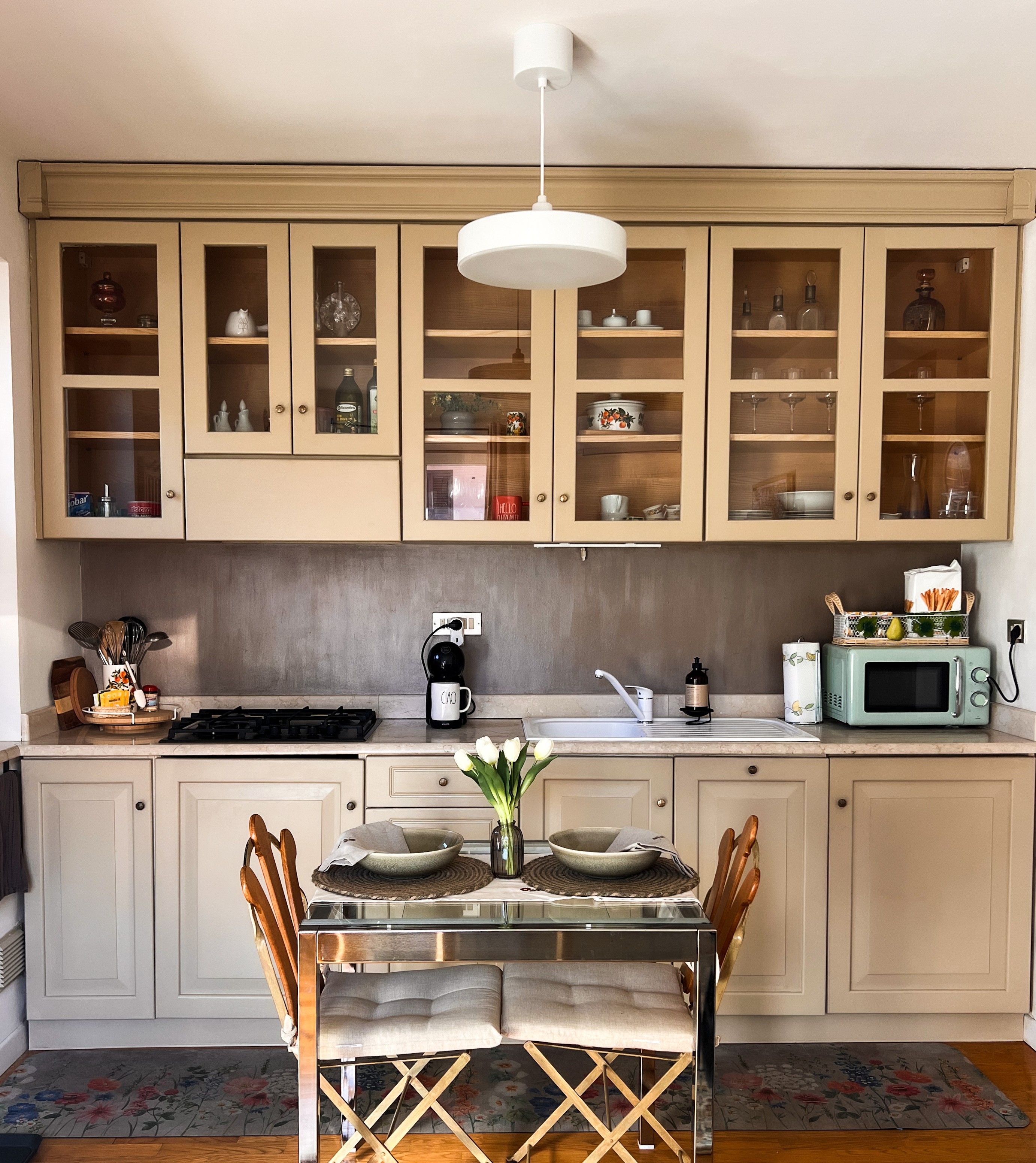 Una cocina con armarios de madera, estufa a gas, cafetera, microondas y una mesa de comedor con sillas.