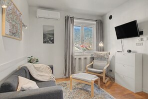 Un soggiorno moderno con un divano grigio, una sedia in legno, un tavolino, una TV a parete e una finestra con tende.