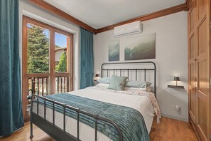 A bedroom with a bed, a window, a door, and a wall-mounted air conditioner.