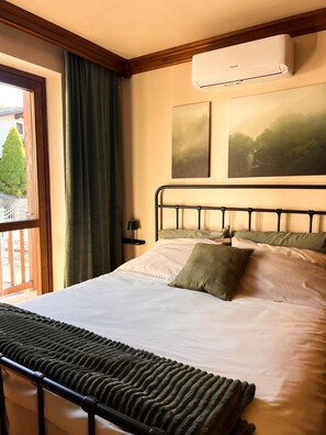 Ein Hotelzimmer mit Bett, einem Fenster mit Vorhängen, einer Klimaanlage und zwei gerahmten Bildern an der Wand.