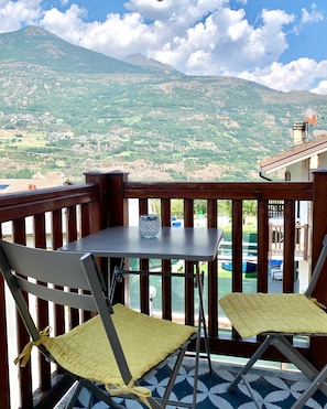 Ein Balkon mit zwei Stühlen und einem Tisch, mit Blick auf eine gebirgige Landschaft.