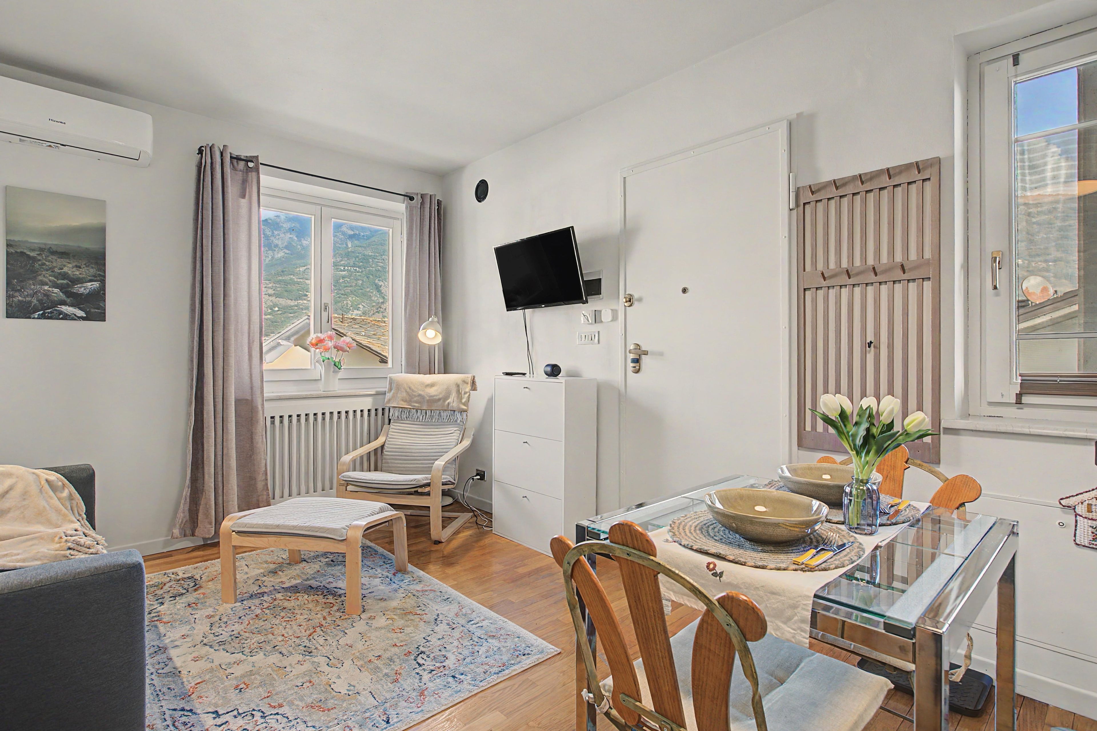 A room with a bed, a chair, a table with a vase, and a television on the wall.