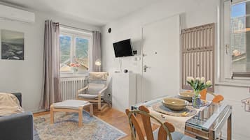 A room with a bed, a chair, a table with a vase, and a television on the wall.
