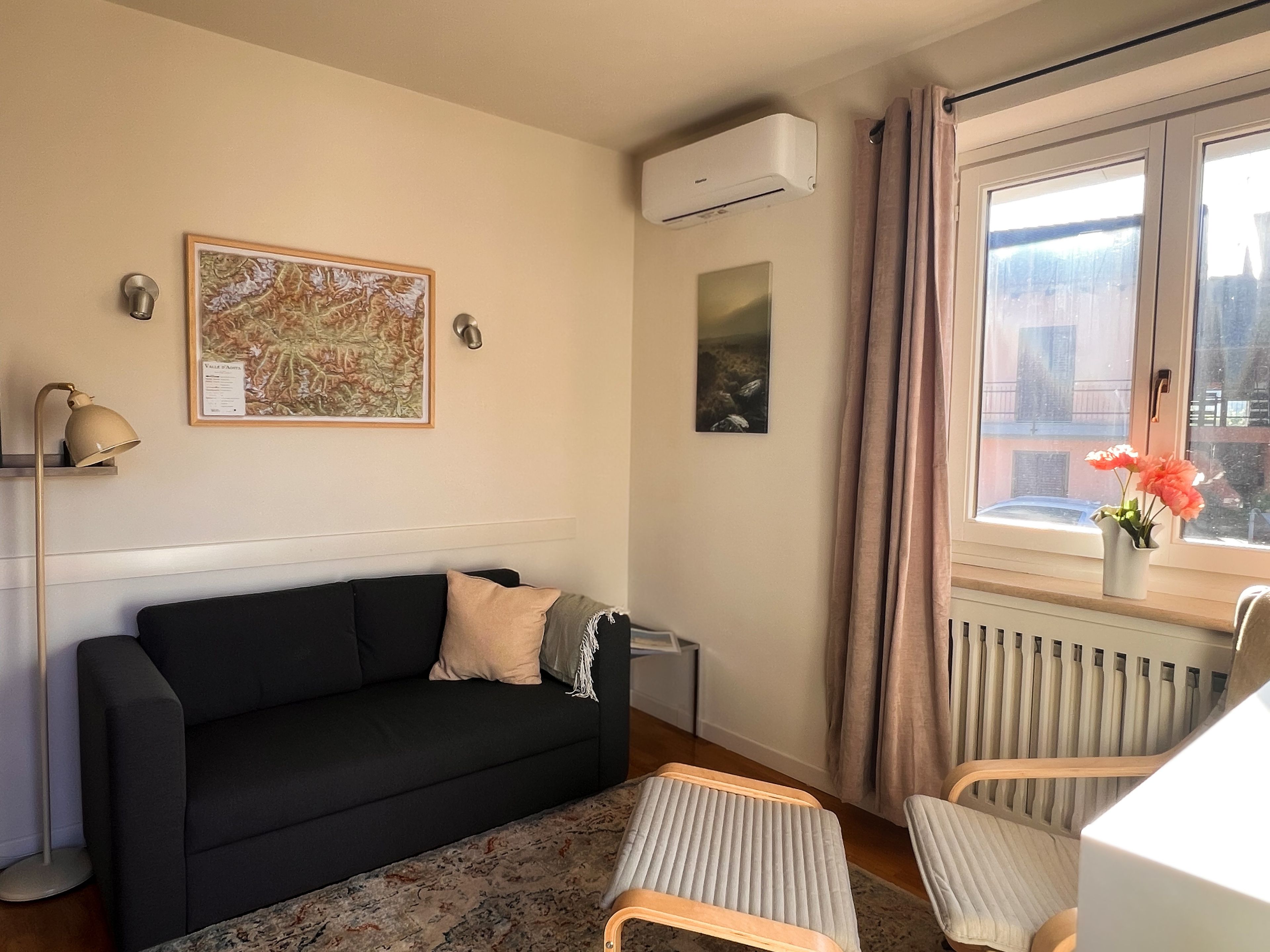 Una sala de estar con un sofá negro, una mesita, una lámpara de pie, un radiador y una ventana con cortinas.