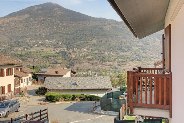 A residential area with a mountain in the background, houses with sloped roofs, and a street with parked cars.