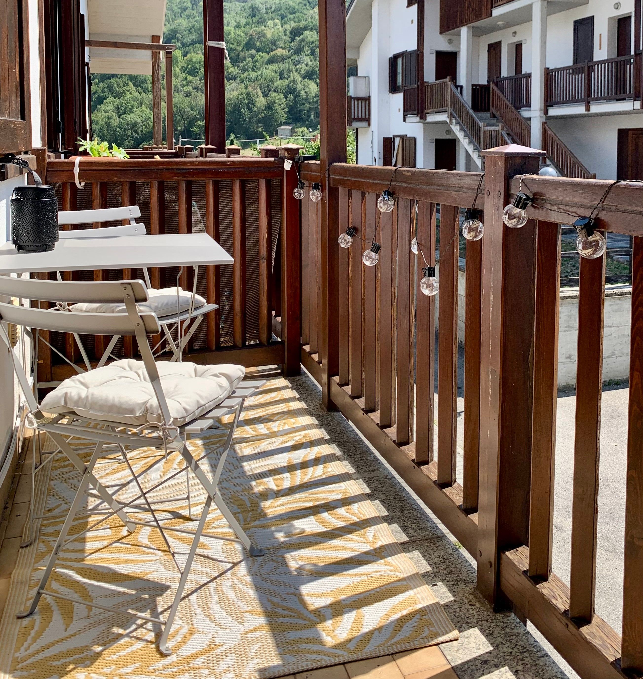 Ein Balkon mit Tisch und Stühlen, einem gemusterten Teppich und einem Holzzaun.