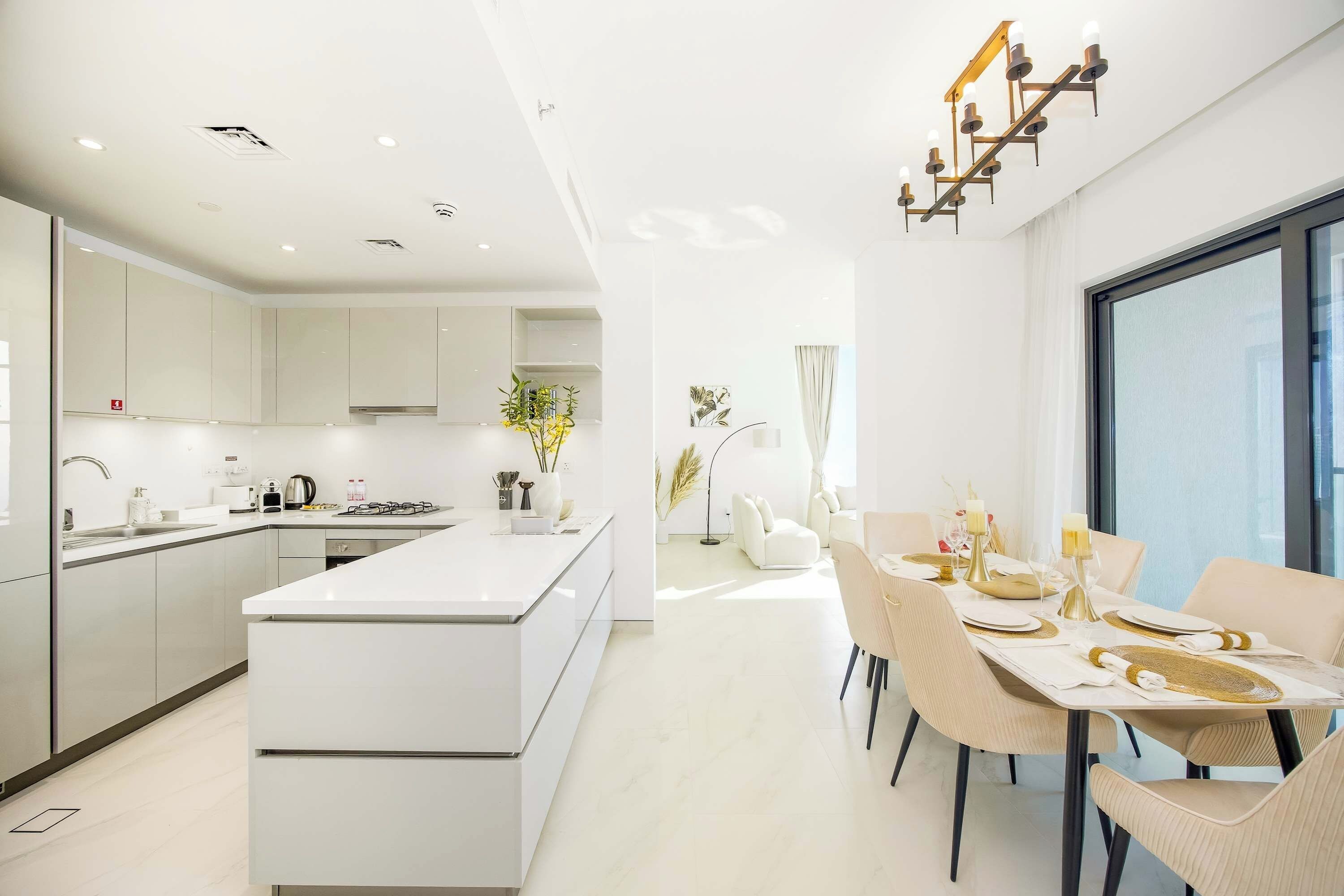 Een moderne keuken met een centraal eiland, een eethoek met een tafel voor vier personen, en een groot raam dat zorgt voor veel daglicht.