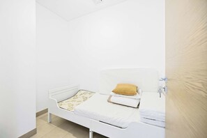 A small, single-bed room with a white headboard, a patterned bedspread, and a single pillow. - Sobha Waves 1BR · Pool & Gym · MBR City (Dubai)