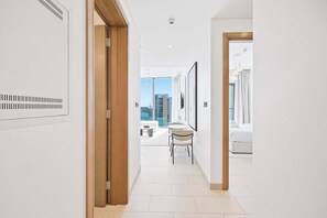 A hotel corridor with a view of the cityscape, a seating area with tables and chairs, and a bed with neatly folded towels. - Sobha Waves 1BR · Pool & Gym · MBR City (Dubai)