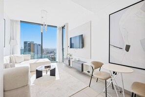 A modern hotel room with a large window, a flat-screen TV, a sofa, a coffee table, and a desk with a chair. - Sobha Waves 1BR · Pool & Gym · MBR City (Dubai)