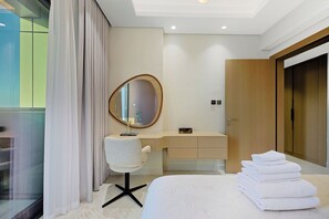 A modern bedroom with a bed, a vanity with a mirror, a chair, and a stack of towels. - Cloud Tower 2BR · Pool & Gym · JVT (Dubai)