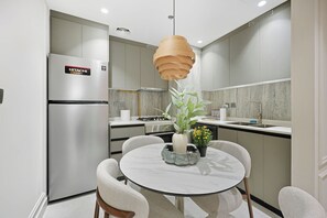 A modern kitchen with a stainless steel refrigerator, a round dining table with chairs, and a hanging light fixture. - Cloud Tower 2BR · Pool & Gym · JVT (Dubai)