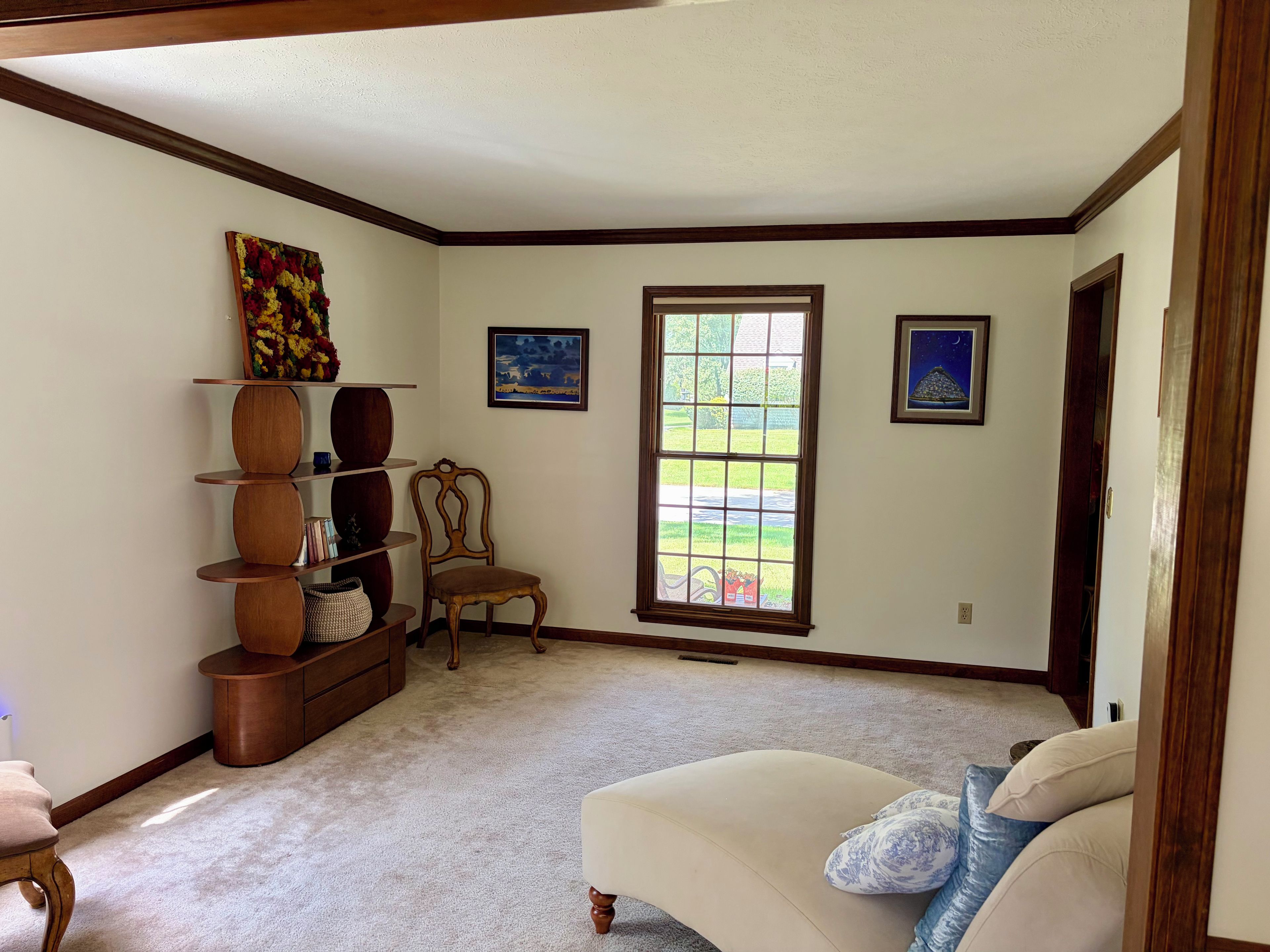 A room with a large window, a chair, a sofa, and a wooden bookshelf.