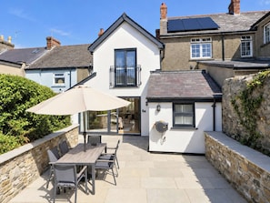 A two-story house with a patio area featuring a table and chairs, a small enclosed space with a window, and a stone wall. - Rheidiol (Haverfordwest)