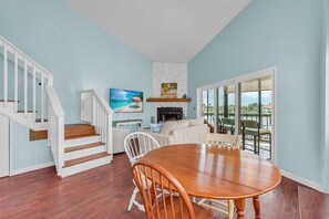 A dining area with a wooden table and chairs, a staircase with white railings, and a view of a body of water through large windows. - Indian Sands B3 (Indian Shores)