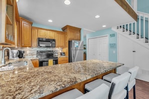A kitchen with granite countertops, wooden cabinets, stainless steel appliances, and a bar area with seating. - Indian Sands B3 (Indian Shores)