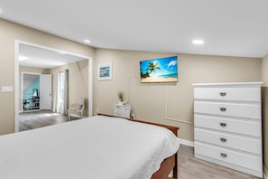 Een slaapkamer met een bed, een dressoir, een televisie aan de muur en een deur naar een andere kamer.
