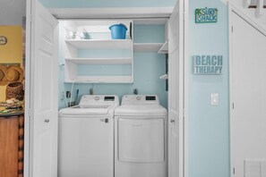 A laundry room with two white washing machines, a blue bucket on a shelf, and a sign that reads 'SURF SHACK' on the wall. - Indian Sands B3 (Indian Shores)