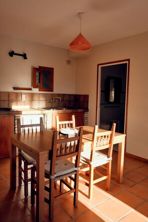A dining area with a wooden table and chairs, a kitchen with a tiled backsplash, and a hanging light fixture. - Hierbabuena Apartment – Perfect for Families (Vejer de la Frontera)