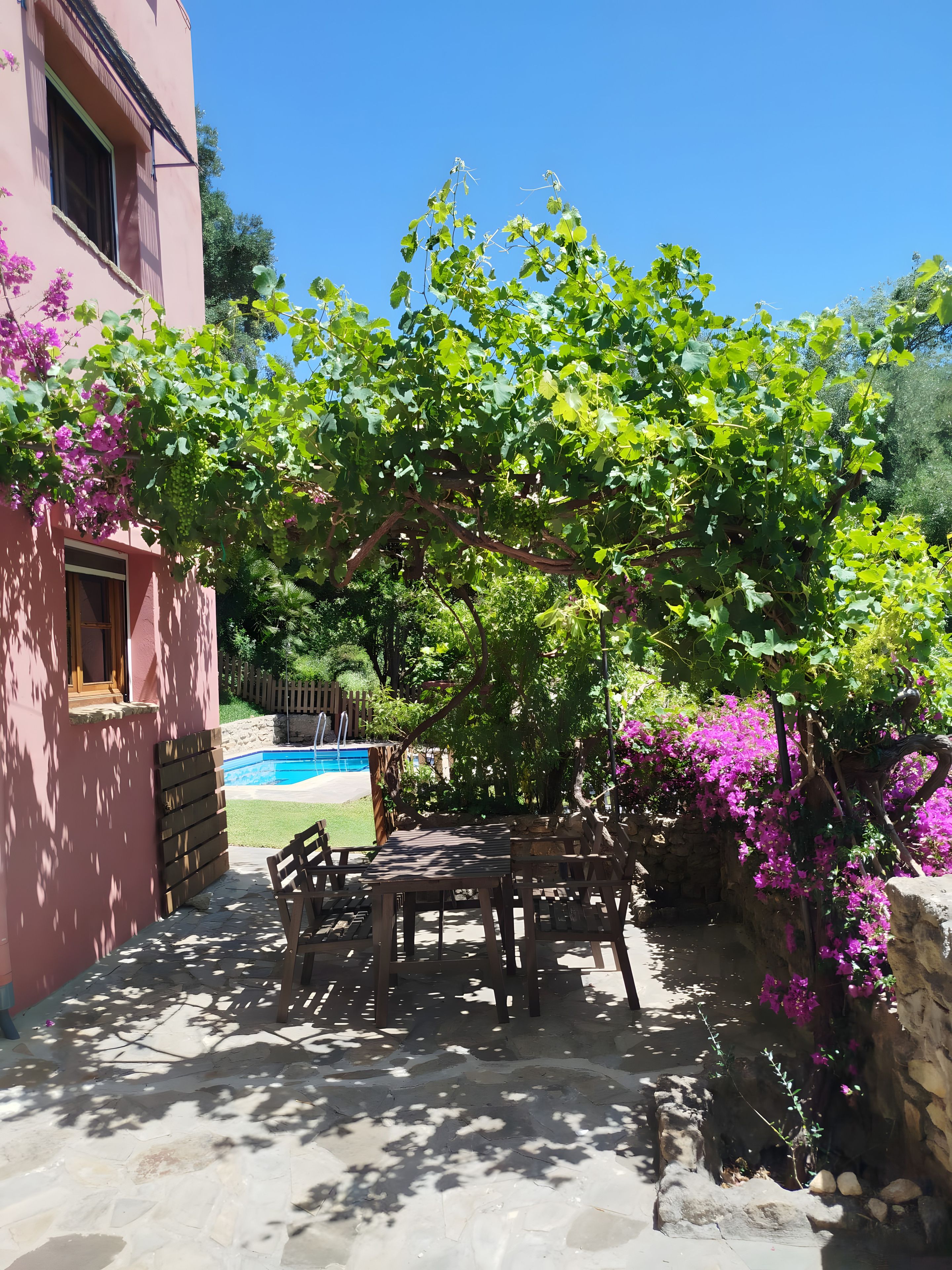 Eine Terrassenfläche mit Tisch und Stühlen, ein Schwimmbecken und ein rosafarbenes Gebäude.