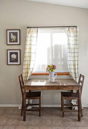 A dining area with a wooden table and chairs, a window with blinds, and two framed pictures on the wall. - Cozy Duplex by Portal Park | Pet Friendly (Colorado Springs)