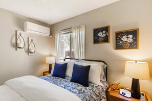 Ein Hotelzimmer mit Bett, Nachttischlampen, Klimaanlage, einem Fenster mit Vorhängen und zwei an der Wand befestigten Bildern.