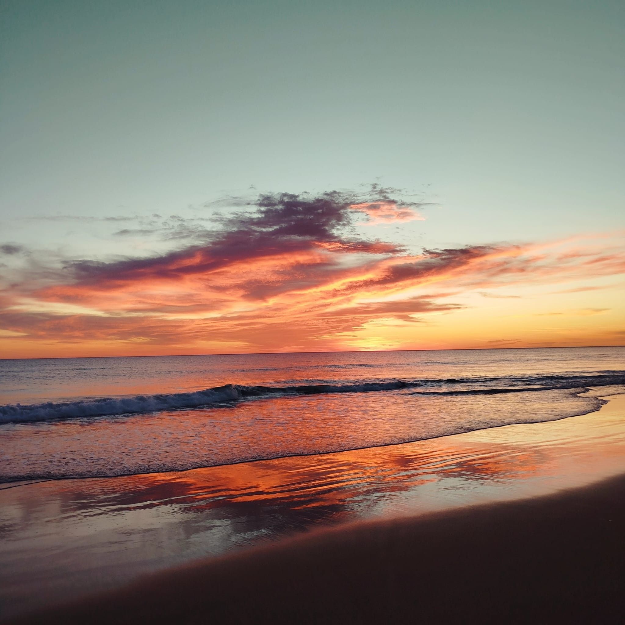 A beach with waves and a sunset.