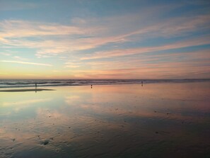 Ein Strand mit ruhiger See, blauem Himmel und einer Person, die am Sand entlanggeht.