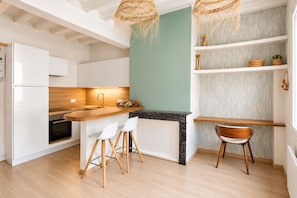 Una cocina moderna con muebles blancos, encimera de madera y salpicadero negro. Hay dos sillas blancas y un taburete de madera.