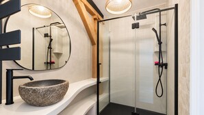 A modern bathroom with a stone sink, a glass-enclosed shower, and a wooden ceiling beam. - Harmoni Studio (Chartres)