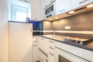 A modern kitchen with white cabinetry, a built-in oven, a microwave, and a gas stove. - Le Sunset - station de ski accessible à pied (Chamrousse)