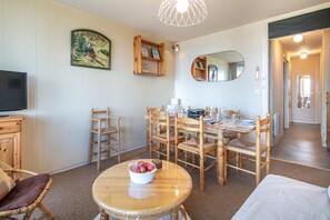 A dining area with a round table, chairs, a television, and a painting on the wall. - Le Sunset - station de ski accessible à pied (Chamrousse)