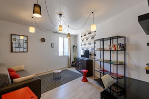 Un soggiorno moderno con un divano, uno sgabello rosso, una libreria e un televisore su un mobile.
