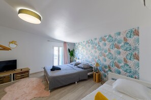 Ein Schlafzimmer mit einem Bett, einem Fernseher, einer Holzkommode, einem rosa Teppich und einer Wand mit tropischen Blättermotiven.