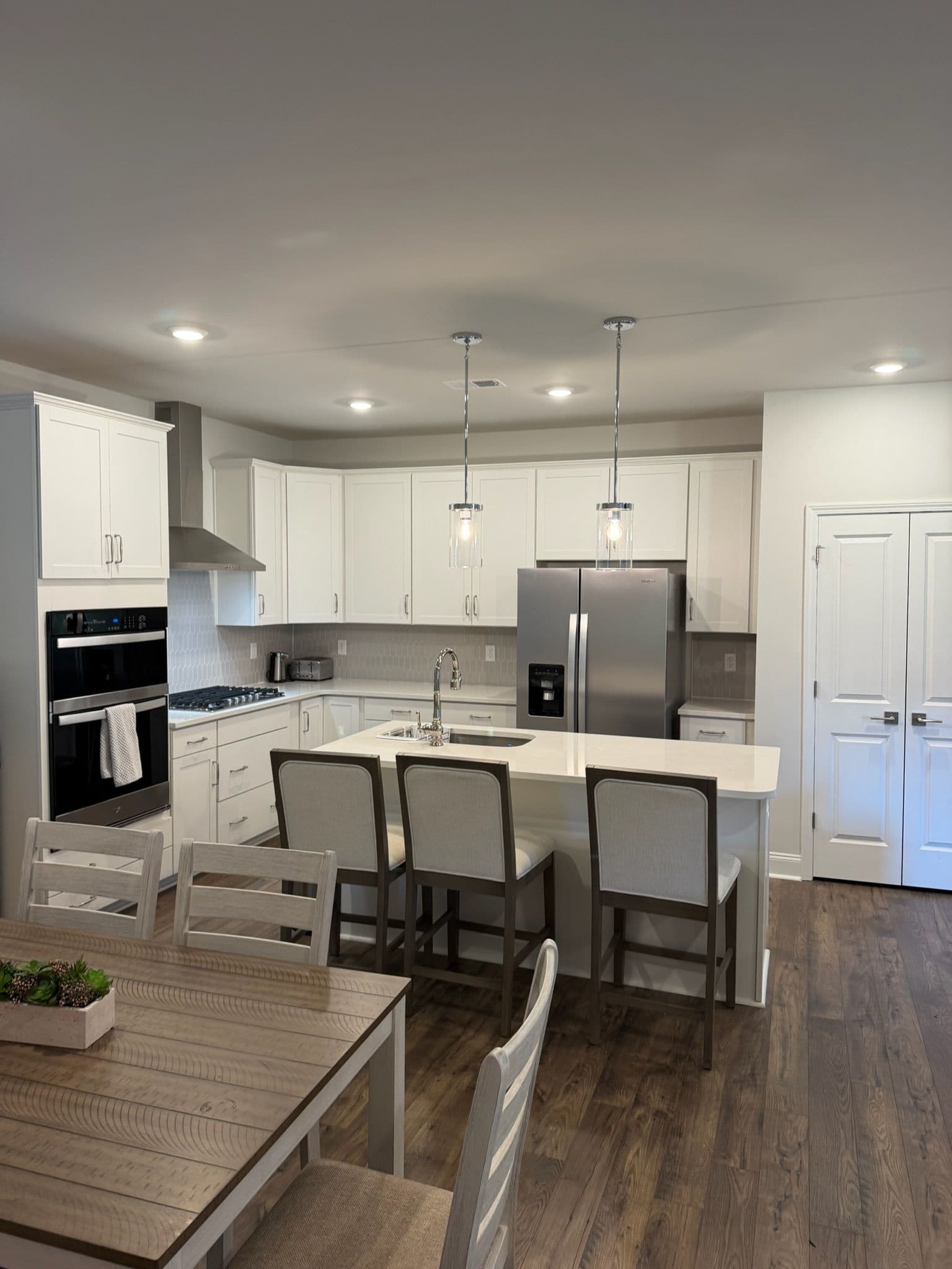 A modern kitchen with white cabinetry, stainless steel appliances, a central island with seating, and pendant lighting.