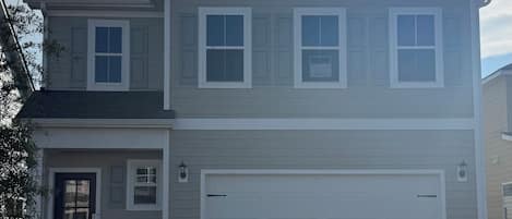 A two-story residential building with a garage, a front door, and a small front yard.