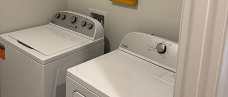 A laundry room with two front-loading washers and dryers, a shelf with a basket and a bottle, and a framed picture on the wall.