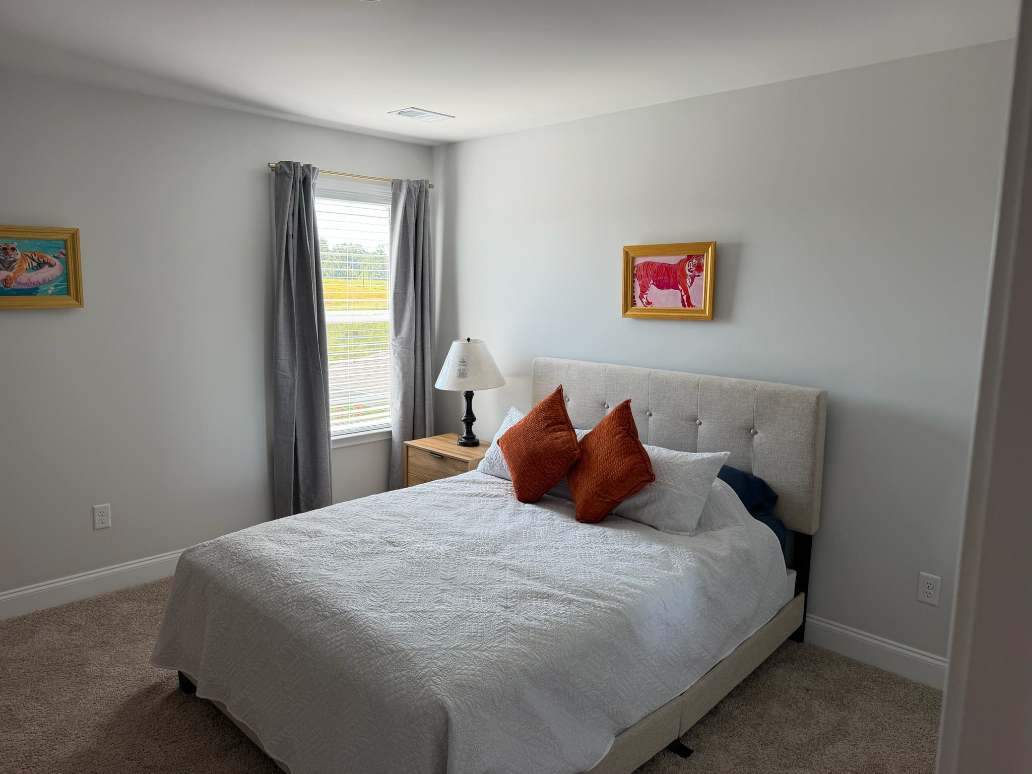 Quarto com cama, mesa de cabeceira, abajur e duas imagens emolduradas na parede.