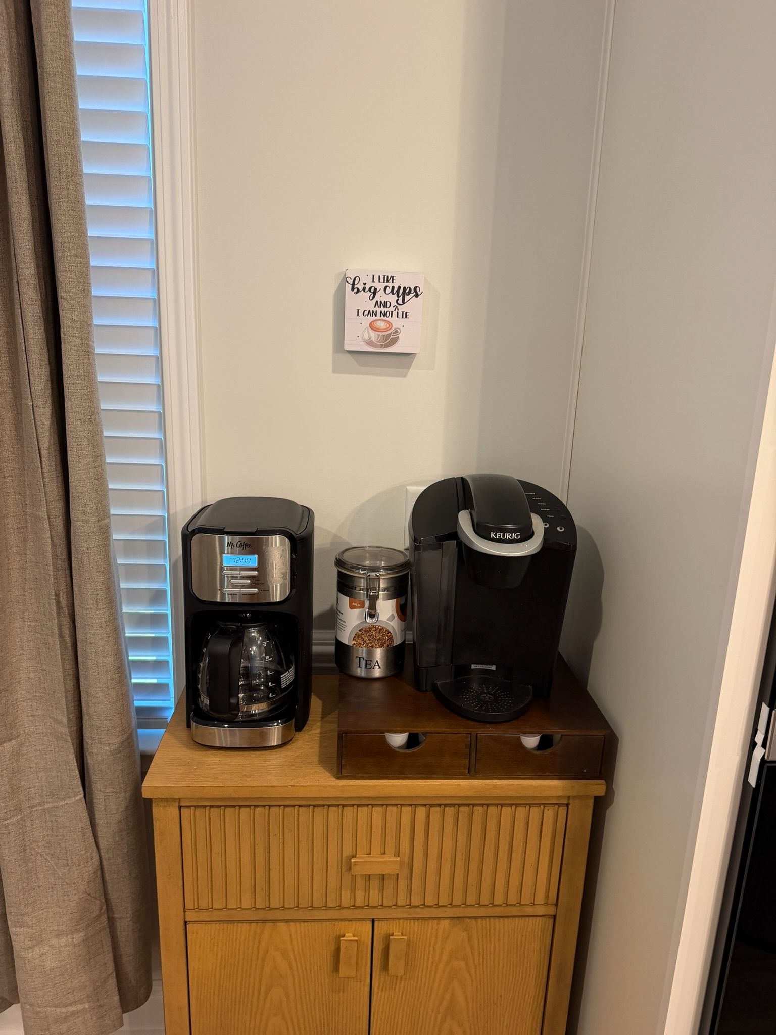 Uma cafeteira, uma Keurig e um recipiente para chá sobre um armário de madeira.