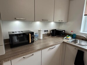 A compact kitchenette with a microwave, toaster, kettle, and a sink. - Duthie Gardens Retreat – Peterhead (Aberdeenshire)