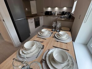 Ein Essbereich mit einem Holztisch, gedeckt für vier Personen, komplett mit weißen Tellern, Schüsseln, Besteck und Gläsern.