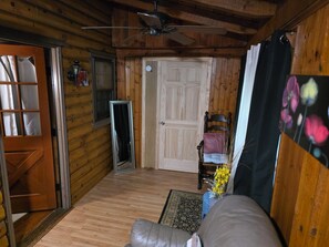 A log cabin interior with a ceiling fan, a wooden door, a mirror, a chair with cushions, and a rug.