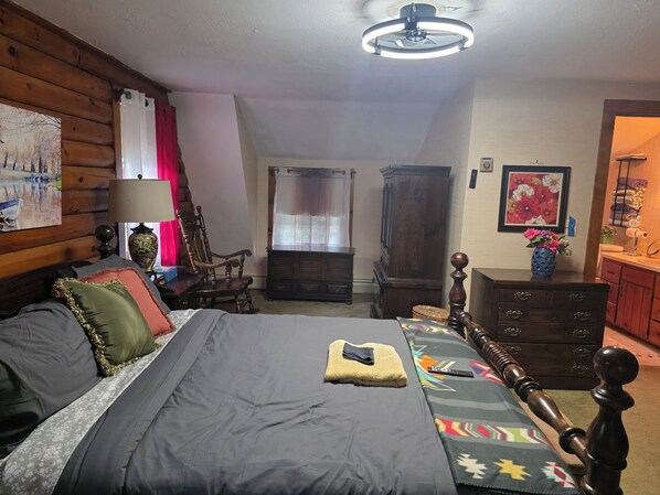 A bedroom with a bed, a wooden headboard, a nightstand, a lamp, a chair, a cabinet, and a ceiling fan.