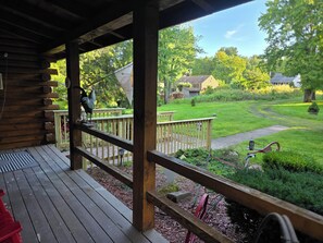 A wooden deck with a railing, a bird sculpture, and a view of a green landscape with a path and a house in the background. - Spacious 5-bedroom Log Cabin style house in gorgeous Bloomfield with AC (Bloomfield)