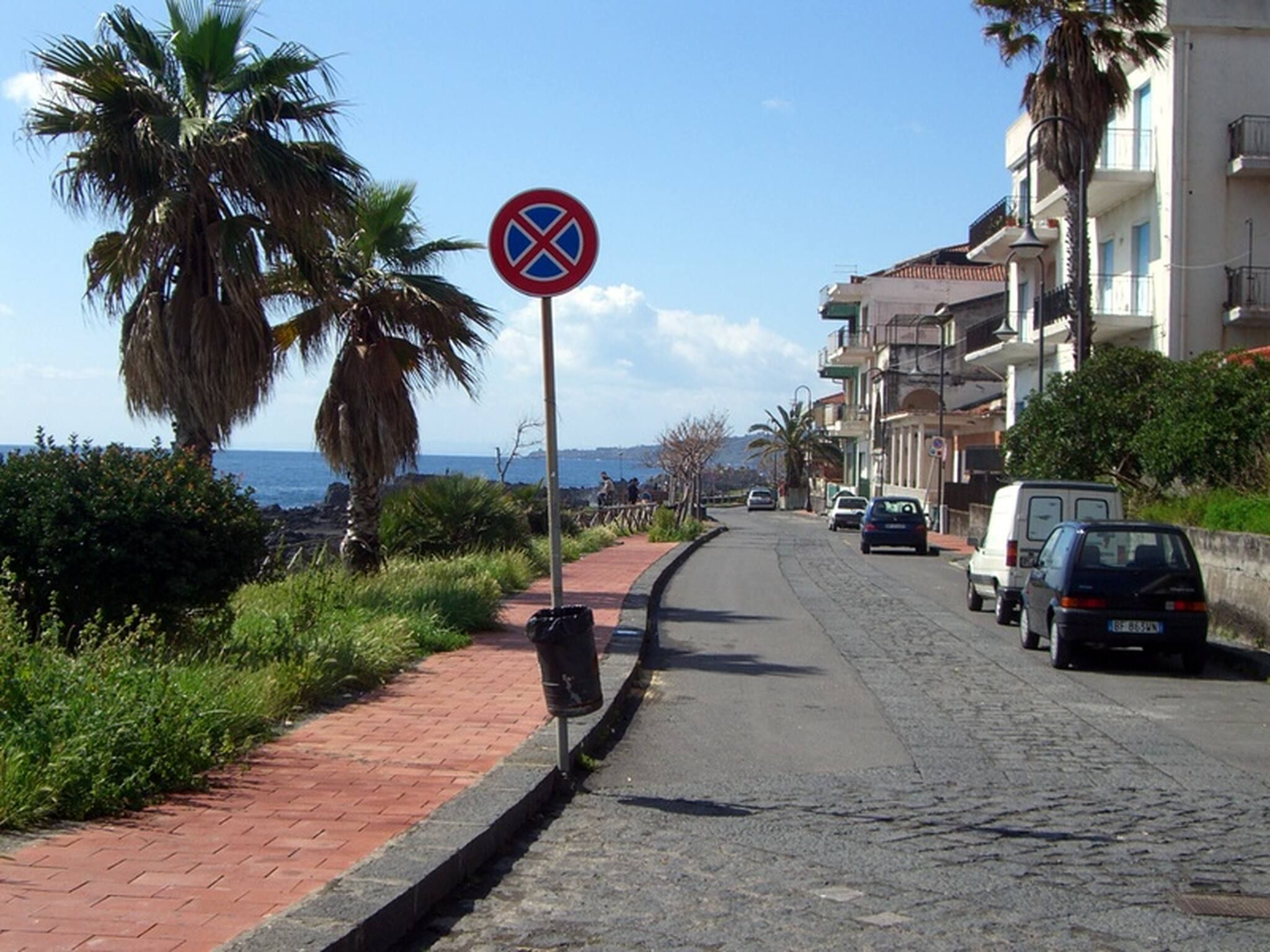 Una calle costera con un cartel de no estacionamiento, palmeras y automóviles estacionados.