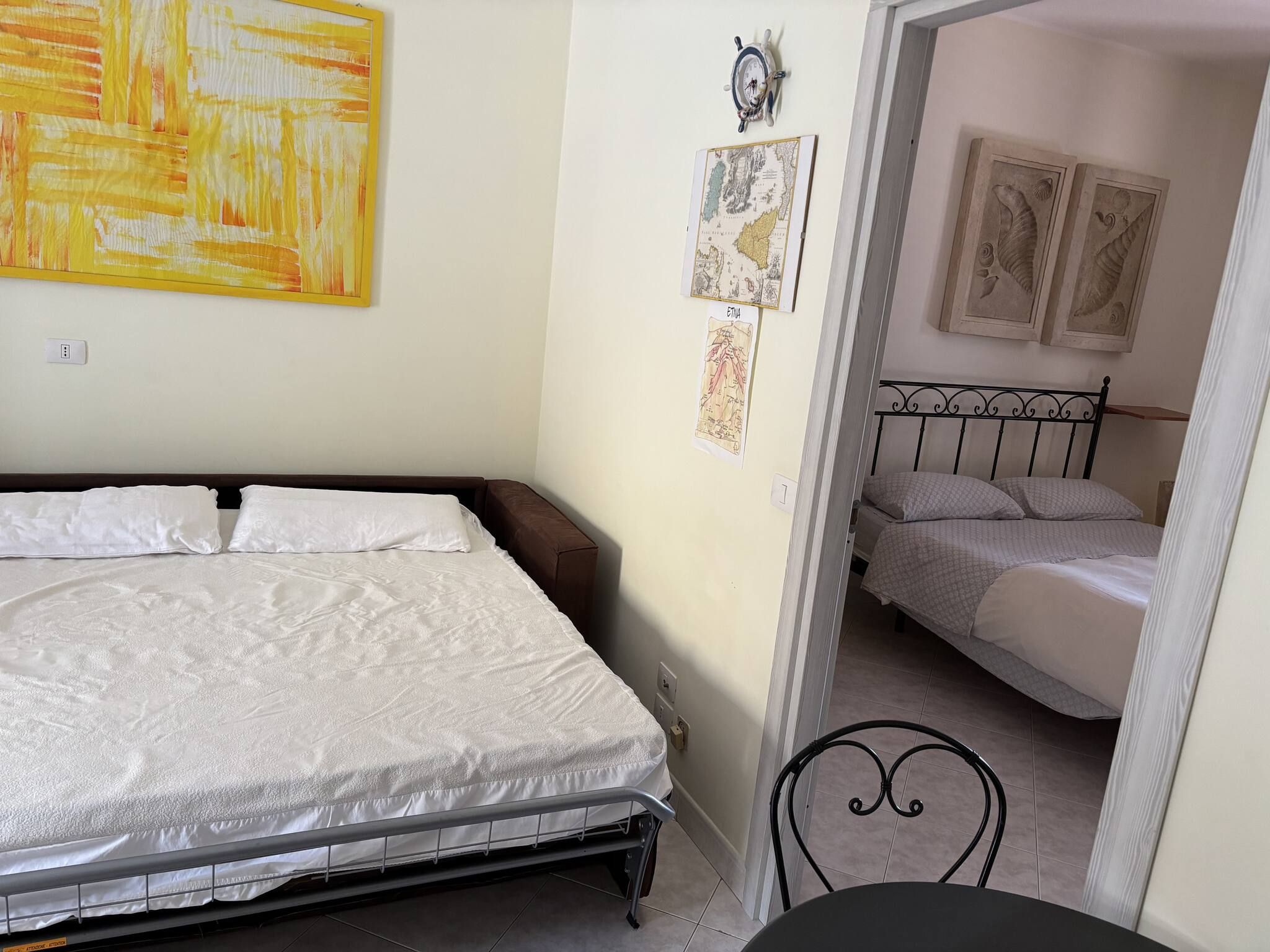 A bedroom with a bed, a nightstand, and a chair. There are wall decorations including a map and a framed picture.
